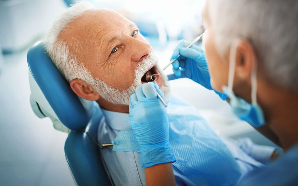 Closeup side view of older man getting a dental exam dental professional is using a scaler and mirror dental cleanings dentist in Palmdale California